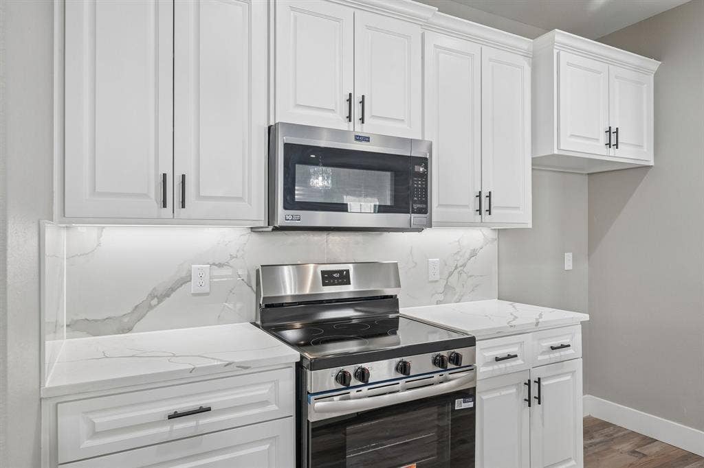 1221 S Rockwall Avenue, Terrell, TX 75160 Kitchen featuring white shaker-style cabinetry, matte black hardware, integrated stainless steel appliances, stone-patterned backsplash, and matching stone-patterned countertops