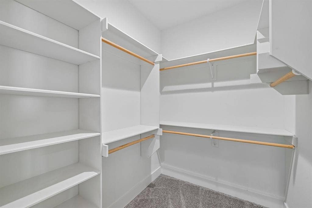 1221 S Rockwall Avenue, Terrell, TX 75160 Walk-in closet featuring white built-in shelving, wooden garment rods, and carpeted flooring