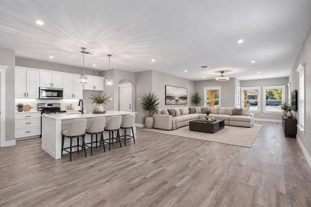 1221 S Rockwall Avenue, Terrell, TX 75160 Open concept living area featuring wood-finish flooring, white cabinetry, center island with stone countertop, stainless steel appliances, and recessed lighting