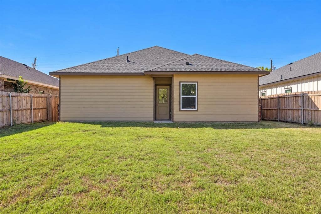 1221 S Rockwall Avenue, Terrell, TX 75160 Exterior rear elevation featuring horizontal siding, a hipped roof, a single-entry door with glass insert, and a fenced backyard with grass lawn