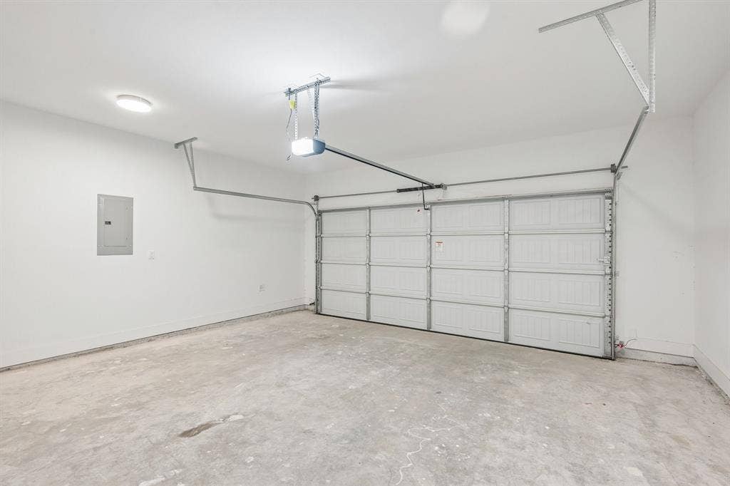 1221 S Rockwall Avenue, Terrell, TX 75160 Two-car garage featuring a sectional door, automatic opener, concrete flooring, and an integrated electrical service panel