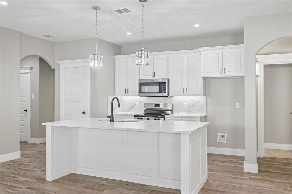 1221 S Rockwall Avenue, Terrell, TX 75160 Kitchen featuring white cabinetry, quartz countertops with a waterfall-edge island, wood-finish flooring, matte black faucet, and arched doorways