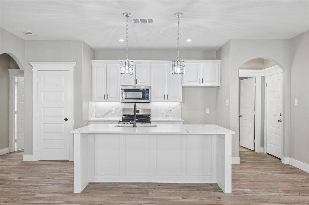 1221 S Rockwall Avenue, Terrell, TX 75160 Kitchen featuring white shaker-style cabinetry, quartz countertops with a waterfall-edge island, stone-patterned backsplash, wood-finish flooring, and dual glass pendant lights