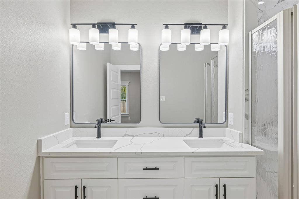 1221 S Rockwall Avenue, Terrell, TX 75160 Double vanity with white cabinetry, matte black hardware, stone-patterned countertop with integrated sinks, dual rectangular mirrors, and multi-light fixtures