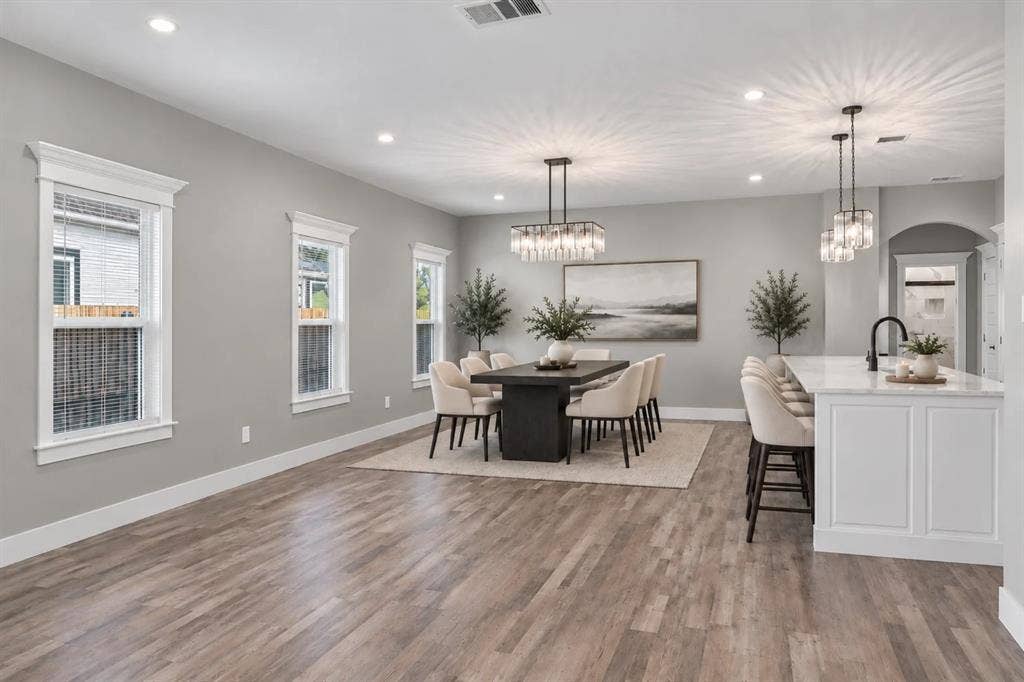 1221 S Rockwall Avenue, Terrell, TX 75160 Open-concept interior featuring wood-finish flooring, recessed lighting, a rectangular tiered crystal chandelier, a center island with white cabinetry and a stone countertop, and multi-pane windows with detailed trim