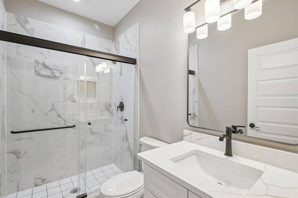 1221 S Rockwall Avenue, Terrell, TX 75160 Bathroom featuring a vanity with a white countertop, a walk-in shower with floor-to-ceiling tiled walls and a glass enclosure, matte black fixtures, and a framed mirror