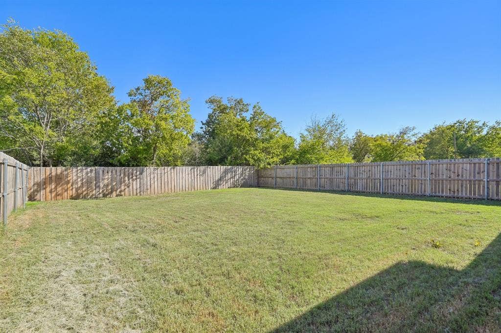 1221 S Rockwall Avenue, Terrell, TX 75160 Expansive backyard featuring a level grass lawn, perimeter wood privacy fencing, and mature trees