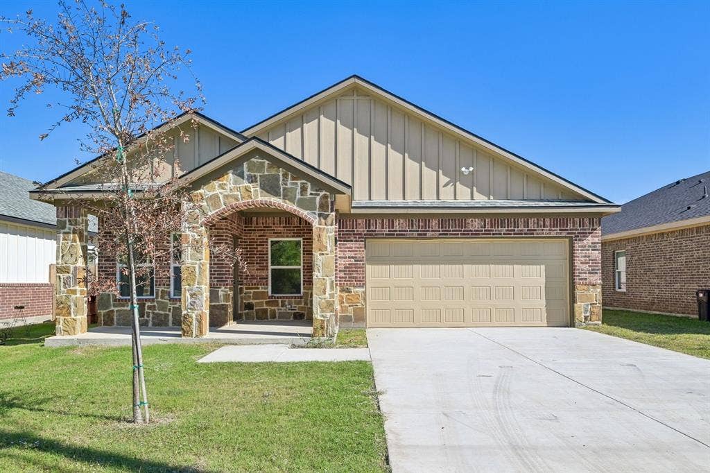 1221 S Rockwall Avenue, Terrell, TX 75160 Single-story exterior featuring a brick and stone facade, vertical siding accents, an arched covered entryway, and a concrete driveway leading to an attached two-car garage