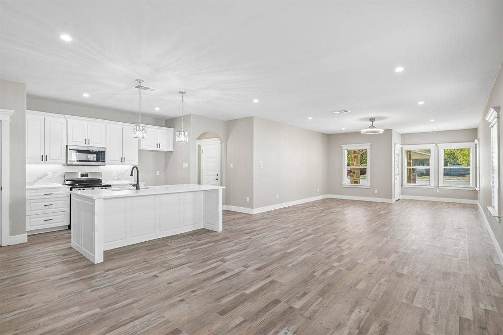 1221 S Rockwall Avenue, Terrell, TX 75160 Open-concept kitchen featuring white shaker-style cabinetry, quartz countertops, a central island, wood-finish flooring, and recessed lighting