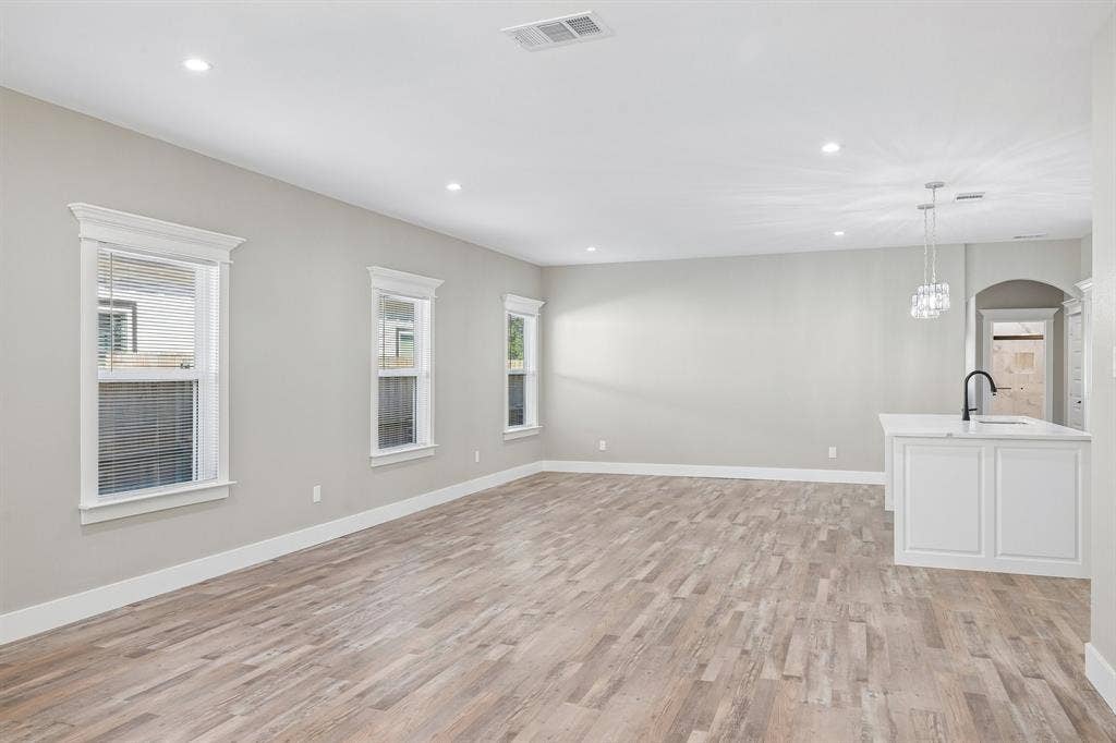 1221 S Rockwall Avenue, Terrell, TX 75160 Open-concept interior featuring wood-finish flooring, recessed lighting, neutral wall tones, multi-pane windows with detailed trim, and a built-in island with a matte black faucet
