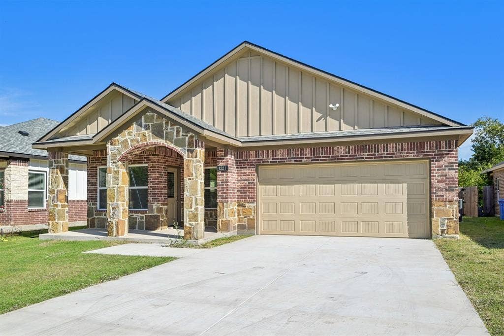 1221 S Rockwall Avenue, Terrell, TX 75160 Exterior featuring brick and stone masonry, vertical siding, a covered entryway with a stone-clad arched porch, and a two-car garage