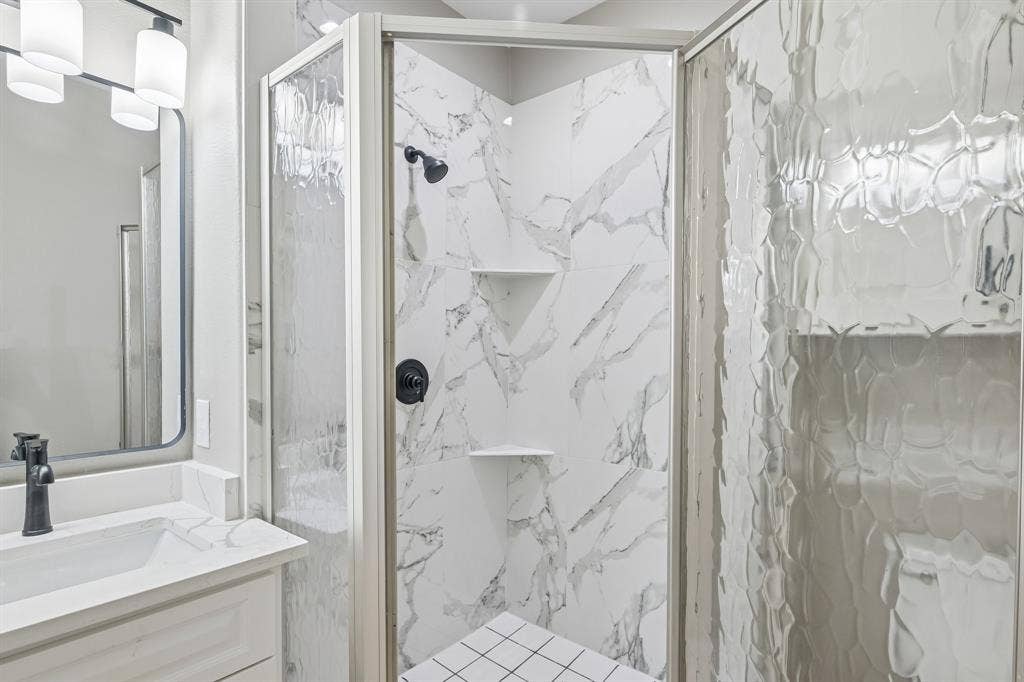 1221 S Rockwall Avenue, Terrell, TX 75160 Corner shower enclosure with textured glass doors and stone-patterned tile surrounds
