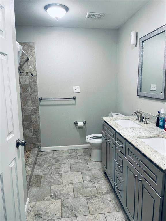 706 E High Street, Terrell, TX 75160 Bathroom featuring a dual-sink vanity with a stone countertop, tile flooring, and a walk-in shower with tiled walls
