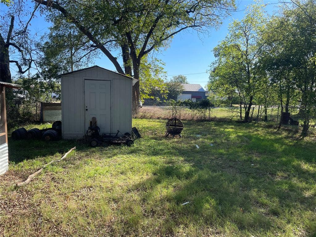 706 E High Street, Terrell, TX 75160 Grassy backyard area featuring mature trees, perimeter chain-link fencing, and a detached storage structure