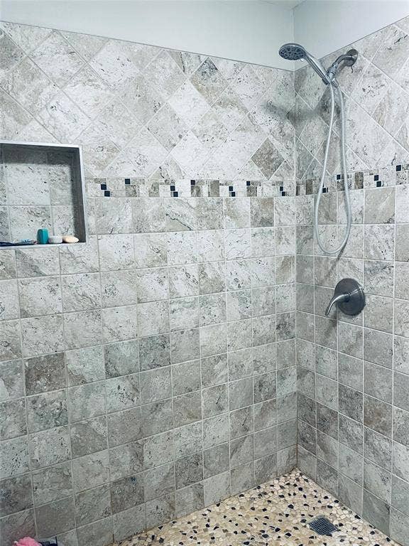 706 E High Street, Terrell, TX 75160 Shower enclosure featuring stone wall tile in a diamond and square pattern, decorative mosaic tile accent, built-in recessed wall niche, and handheld shower fixture
