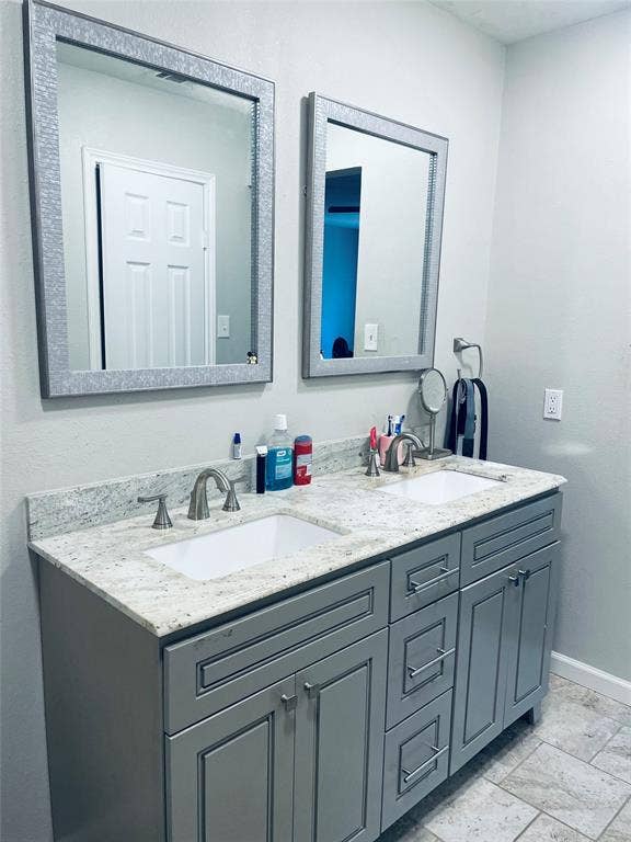 706 E High Street, Terrell, TX 75160 Dual-sink vanity with light-toned stone countertop, rectangular undermount basins, brushed-metal hardware, and decorative framed mirrors