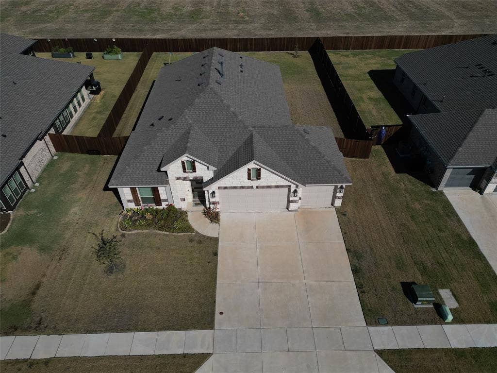 208 Shady Bank Way, Nevada, TX 75173 Aerial perspective of a brick and stone veneer exterior featuring a multi-gable roofline, attached three-car garage, concrete driveway, and full privacy wood fencing