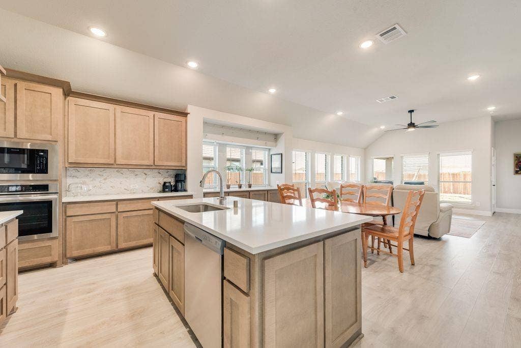 208 Shady Bank Way, Nevada, TX 75173 Kitchen featuring light wood-finish cabinetry, a central island with a solid-surface countertop, stainless steel appliances, and wood-finish flooring under a vaulted ceiling with recessed lighting