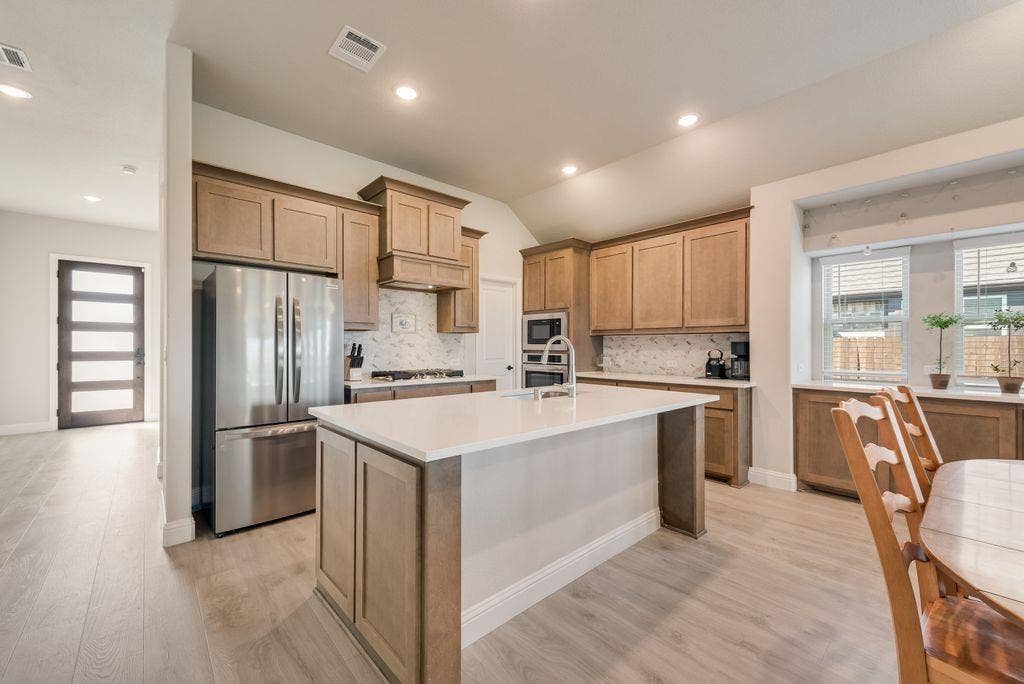 208 Shady Bank Way, Nevada, TX 75173 Kitchen featuring wood cabinetry, a central island with a quartz countertop, stainless steel appliances, and wood-finish flooring