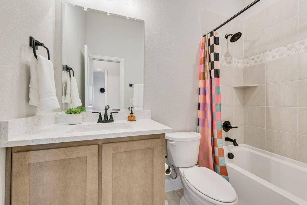 208 Shady Bank Way, Nevada, TX 75173 Bathroom featuring a wood-finish vanity with a stone countertop, an integrated rectangular sink, matte black hardware, and a tub-shower combination with ceramic tile surround