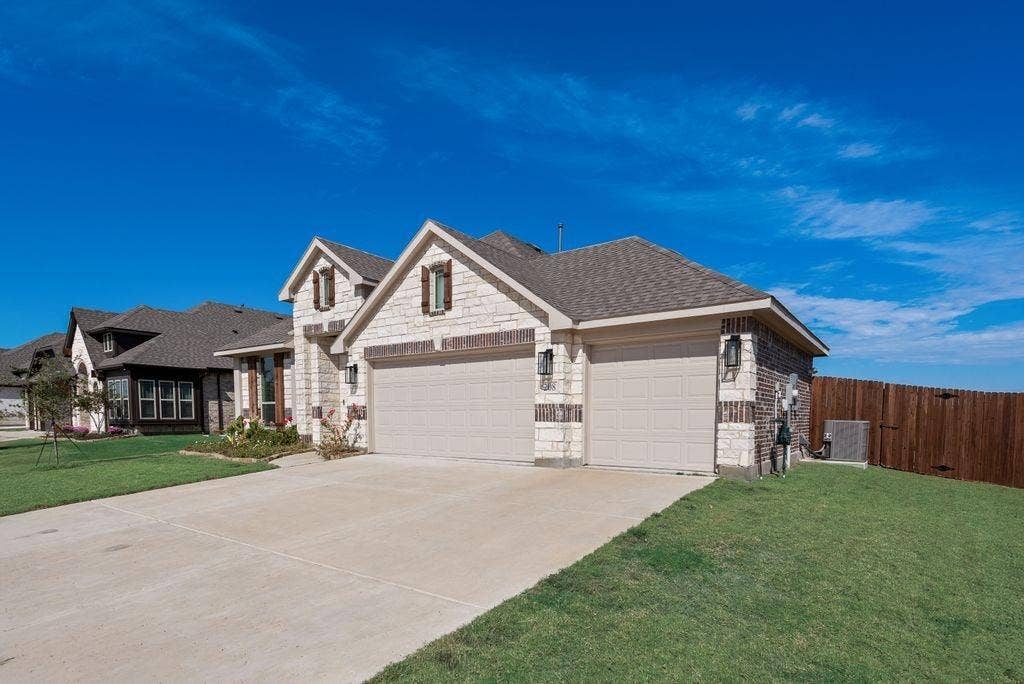 208 Shady Bank Way, Nevada, TX 75173 Stone and brick exterior facade featuring a three-car garage, steep roof lines, decorative window shutters, and exterior wall-mounted lighting