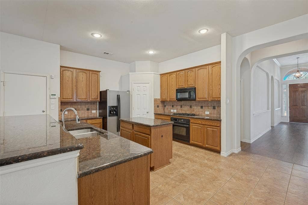 1021 Cherry Hill Lane, DeSoto, TX 75115 Kitchen featuring a center island, stone-finish countertops, wood-finish cabinetry, built-in black appliances, and recessed lighting