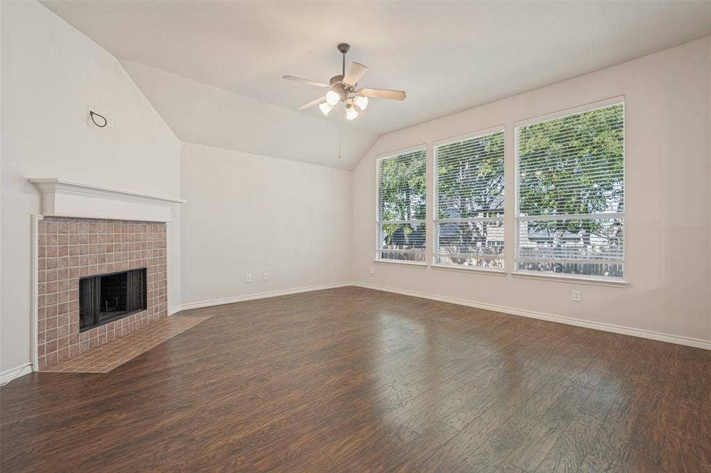1021 Cherry Hill Lane, DeSoto, TX 75115 Vaulted ceilings, wood-finish flooring, fireplace with a tile surround and mantel, and large windows with integrated blinds