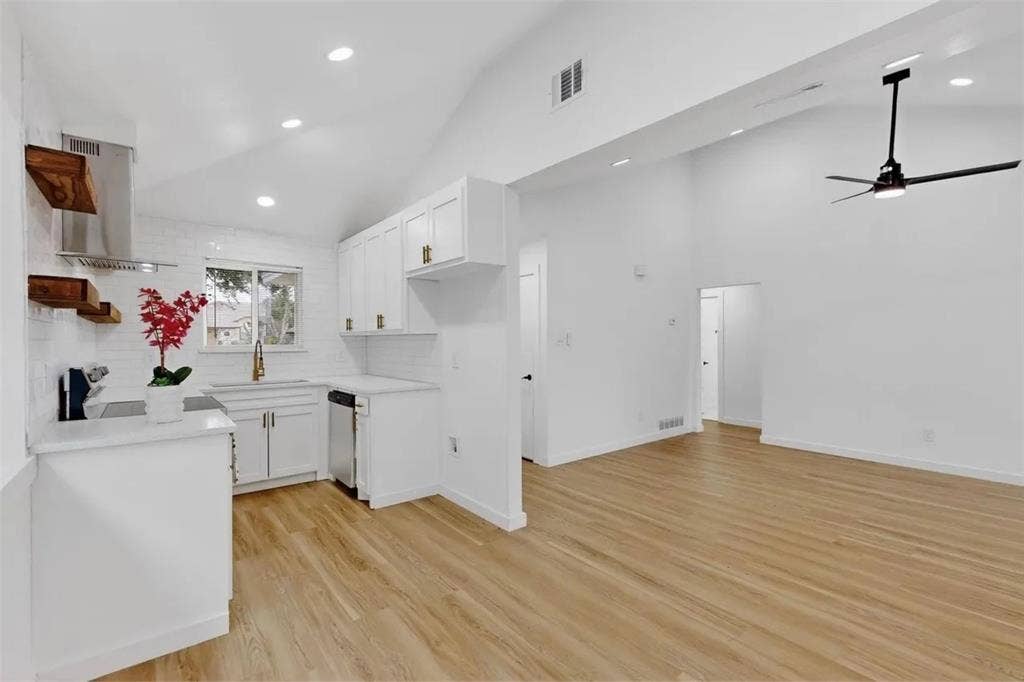 Kitchen featuring wood-finish flooring, vaulted ceilings, white shaker-style cabinetry, open wood shelving, and a stainless steel range hood