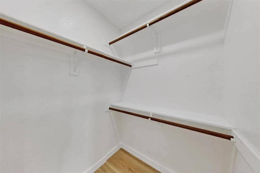 Storage space featuring white shelving and dual-tier hanging rods with wood-finish rails, complemented by wood-finish flooring