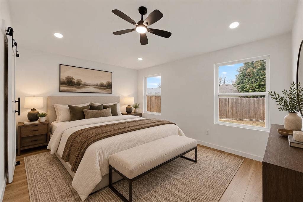 Neutral interior featuring wood-finish flooring, recessed lighting, a matte black ceiling fan, and sliding barn-style door hardware