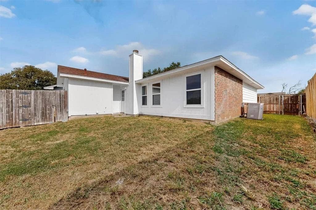Exterior of a single-story residence featuring brick and siding finishes, a prominent masonry chimney, and a private rear yard enclosed by wood fencing