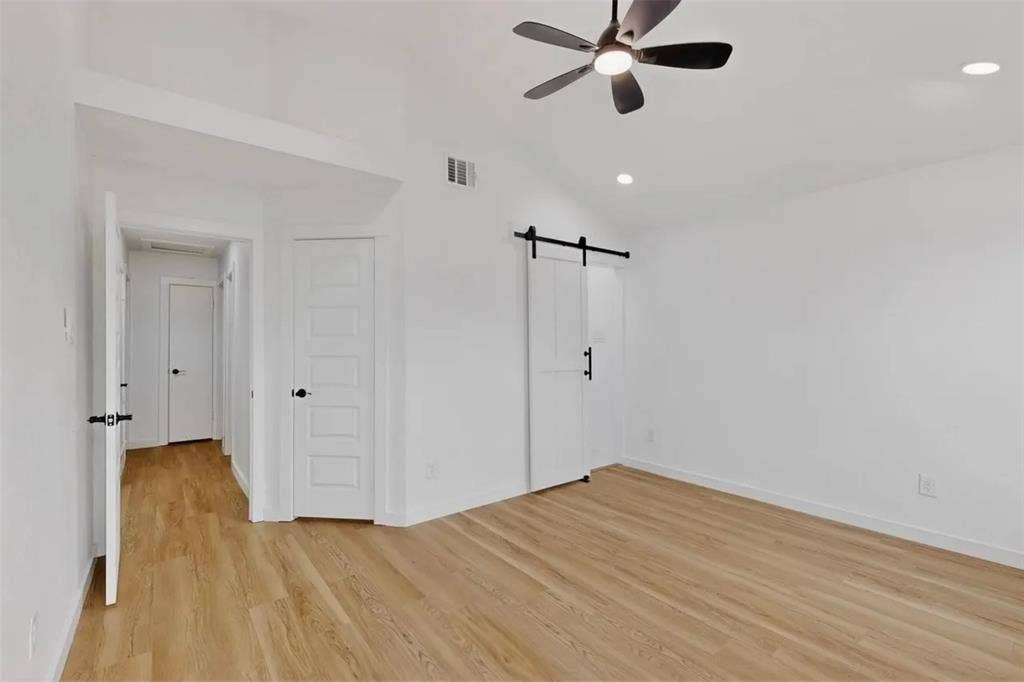 Interior space featuring vaulted ceilings, wood-finish flooring, a contemporary ceiling fan, and a white sliding barn door with matte black hardware