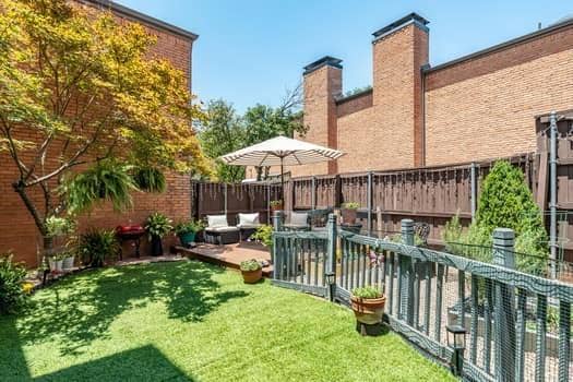 Private outdoor space featuring a brick exterior facade, raised wooden deck, fenced perimeter, and synthetic lawn