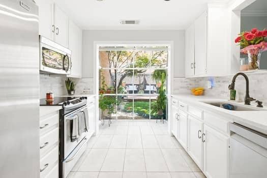 Kitchen featuring white shaker-style cabinetry, stainless steel appliances, tile flooring, stone-tiled backsplash, and floor-to-ceiling glass sliding doors