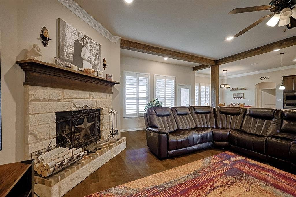 2828 Luke Drive, Farmersville, TX 75442 Stone-faced fireplace with a wood mantel, wood-finish flooring, ceiling fan with light kit, crown molding, and plantation shutters