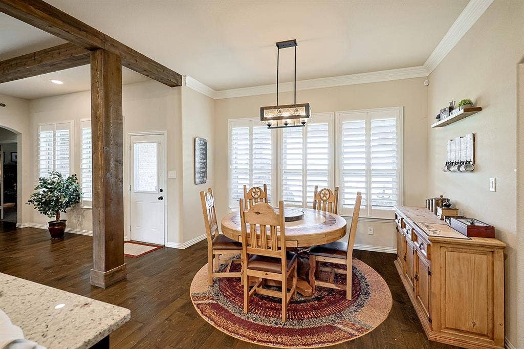 2828 Luke Drive, Farmersville, TX 75442 Dining space featuring wood-finish flooring, exposed stained-wood support beams, custom plantation shutters, crown molding, and a linear multi-light pendant fixture