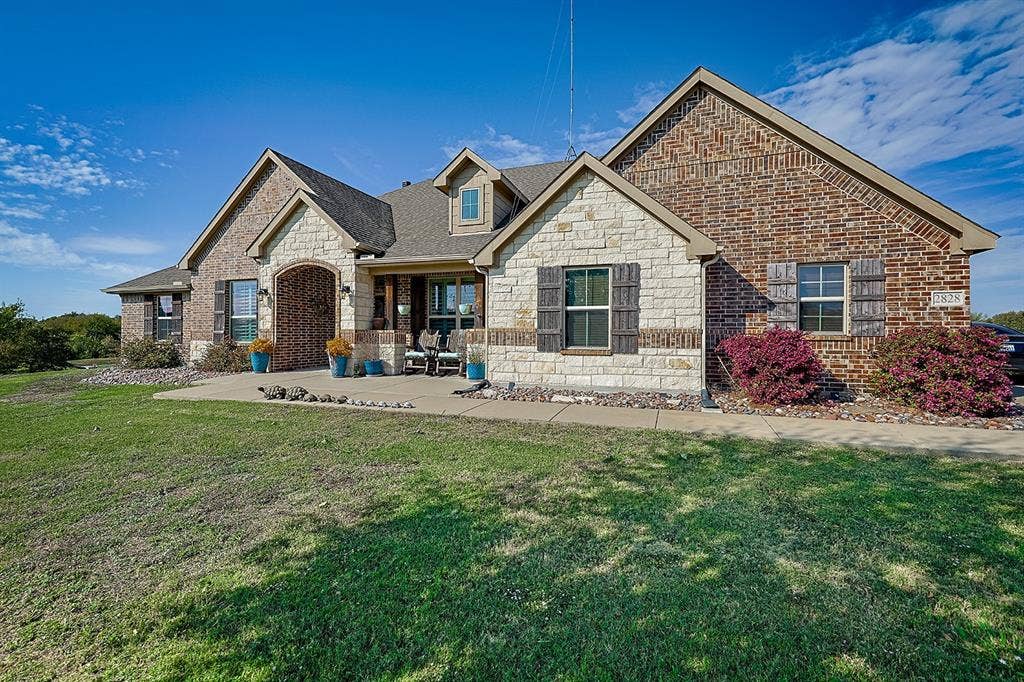 2828 Luke Drive, Farmersville, TX 75442 Multi-gabled exterior featuring a combination of brick and stone masonry, decorative shutter accents, a covered front entry with an arched brick header, and an expansive lawn
