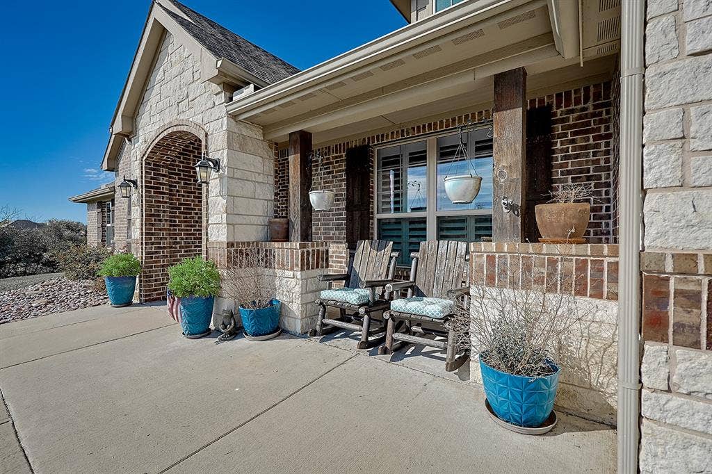 2828 Luke Drive, Farmersville, TX 75442 Covered entryway featuring a stone-clad archway, multi-textured brick and stone exterior, concrete porch, and decorative wood-finish structural posts
