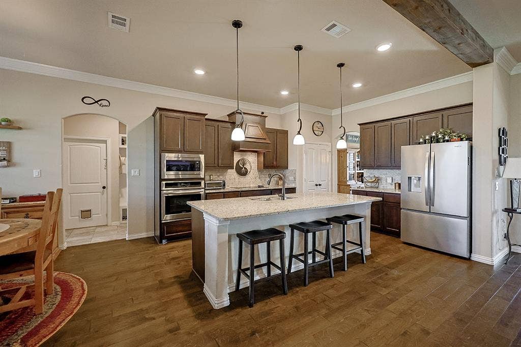 2828 Luke Drive, Farmersville, TX 75442 Kitchen featuring a center island with light-toned stone countertops, dark-stained wood cabinetry, stainless steel appliances, wood-finish flooring, and pendant lighting