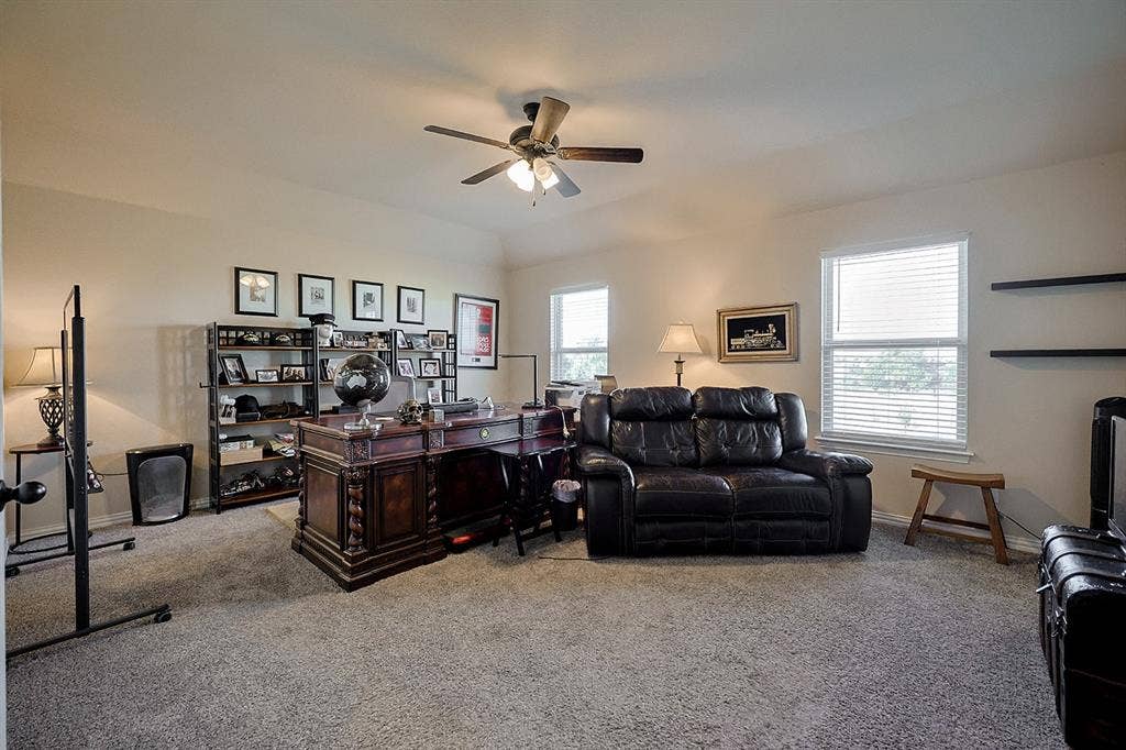 2828 Luke Drive, Farmersville, TX 75442 Neutral-toned carpeted interior featuring a vaulted ceiling, ceiling fan with integrated lighting, and dual wall-mounted floating shelves