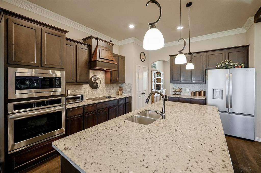 2828 Luke Drive, Farmersville, TX 75442 Kitchen featuring wood cabinetry, stone countertops, a central island with a double-basin stainless steel sink, built-in stainless steel double wall ovens, and pendant lighting