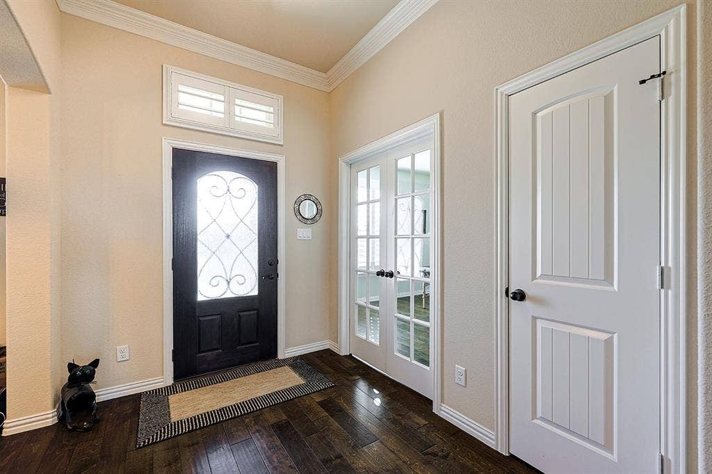 2828 Luke Drive, Farmersville, TX 75442 Foyer featuring wood-finish flooring, crown molding, a dark-finish entry door with decorative glass inlay, transom window with shutters, and dual French doors with glass panes
