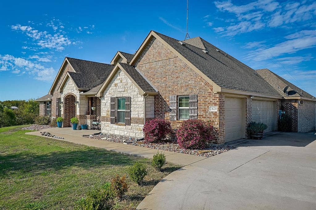 2828 Luke Drive, Farmersville, TX 75442 Multi-gable brick and stone exterior featuring decorative shutters, a concrete driveway, and an attached two-car garage