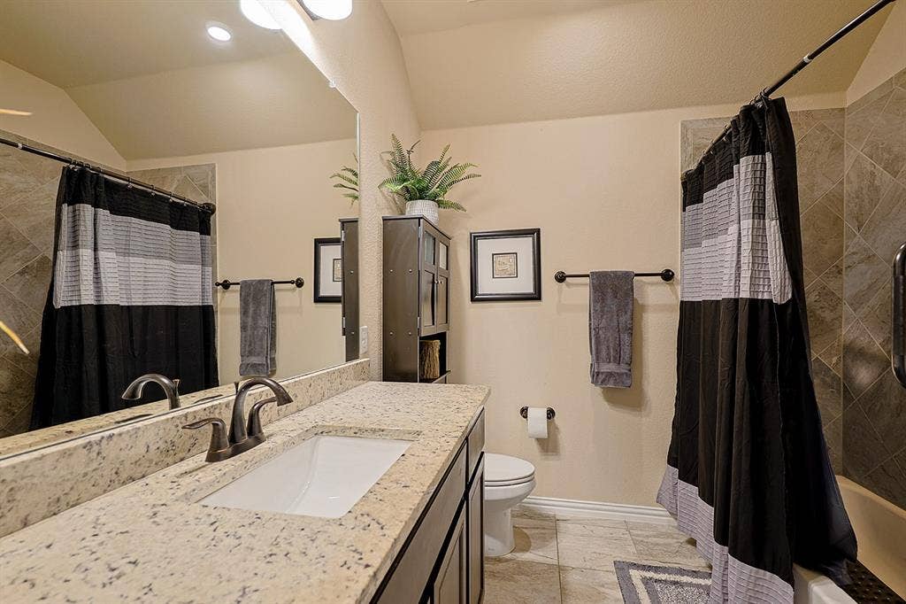 2828 Luke Drive, Farmersville, TX 75442 Bathroom featuring a stone-composite countertop with an integrated rectangular sink, oil-rubbed bronze faucet, large wall-mounted mirror, and tile-surround bathtub