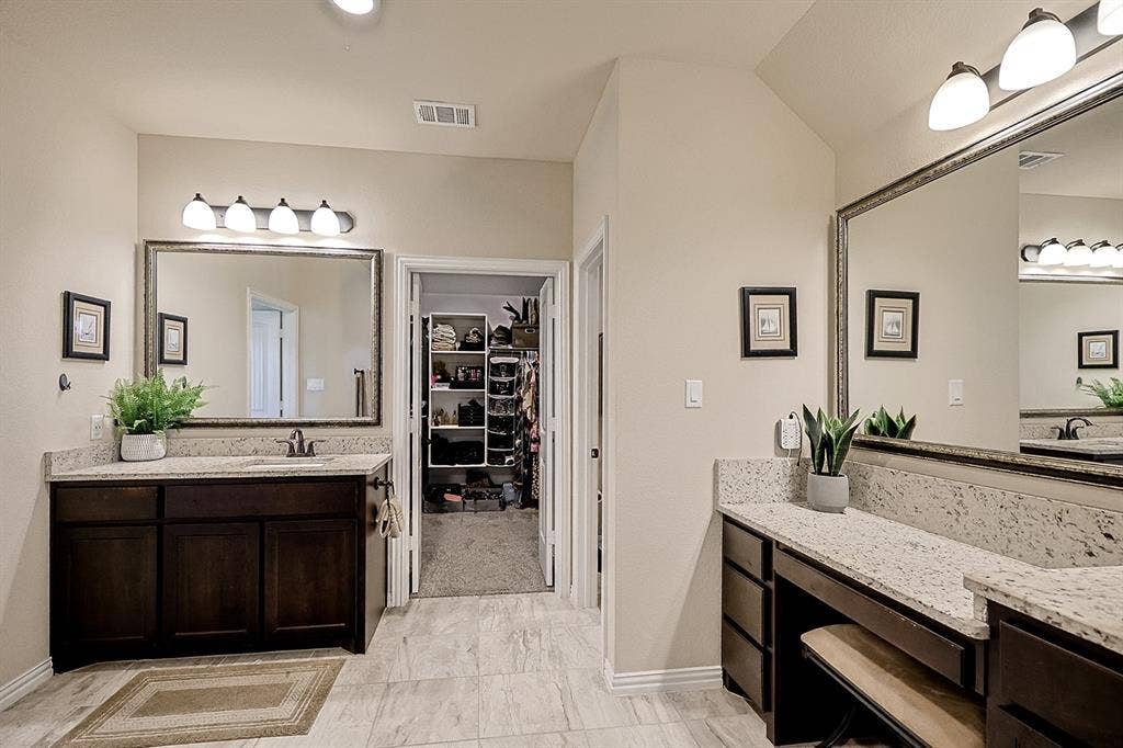 2828 Luke Drive, Farmersville, TX 75442 Bathroom featuring dual dark-finish vanities with stone-look countertops, large framed wall mirrors, four-light vanity fixtures, and tiled flooring