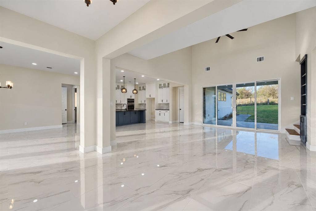 Open-concept interior featuring high ceilings, polished stone-finish flooring, floor-to-ceiling glass sliding doors, and recessed lighting