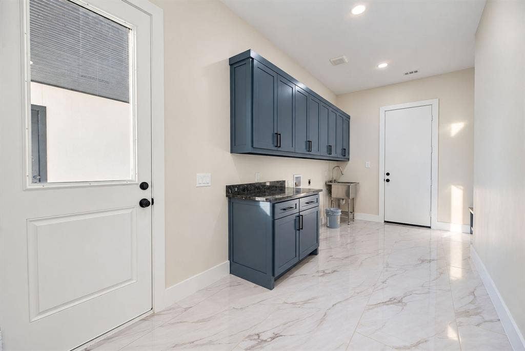 Utility room featuring blue cabinetry, dark stone-finish countertops, recessed lighting, a stainless steel utility sink, and large-format tile flooring