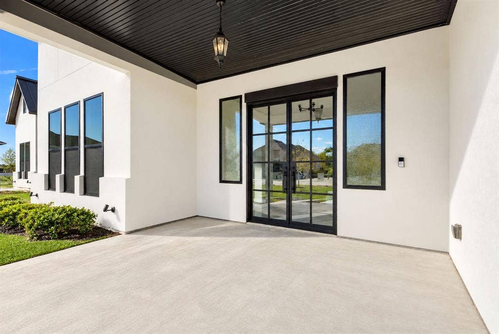 Covered entryway featuring a smooth stucco exterior, dark tongue-and-groove ceiling finish, custom grid-patterned double glass doors, and tall side-light windows