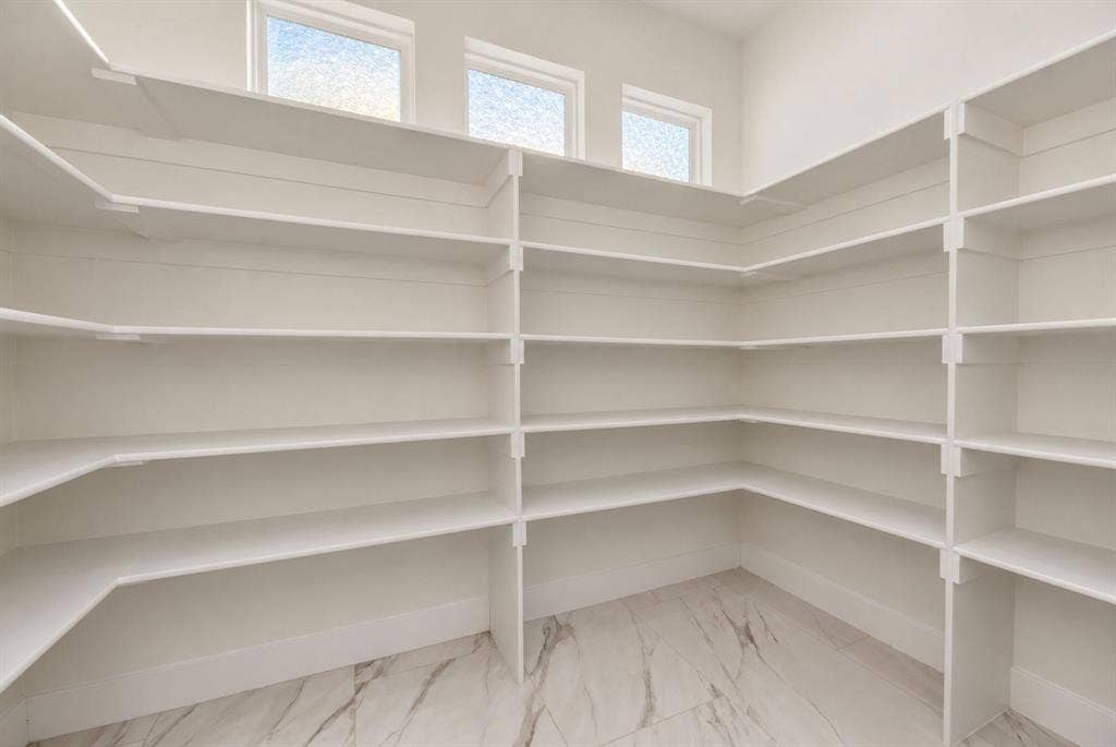 Walk-in pantry featuring white wrap-around shelving, stone-finish flooring, and three high-set windows