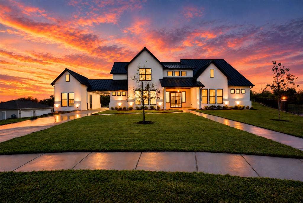Modern residence featuring a white stucco exterior, black metal roof, multi-pane windows, and a covered porte-cochère